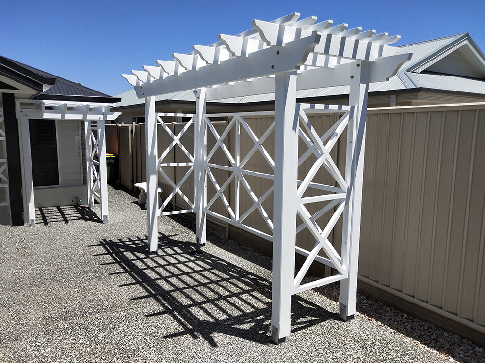 This painted white Pergola has X screening across the back and sides that compliment the design accents of the house.